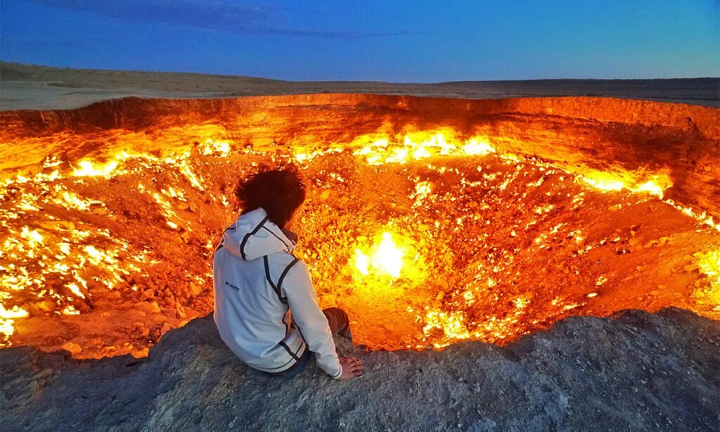 Viajeros observando la Puerta del Infierno, rodeados de un resplandor misterioso.